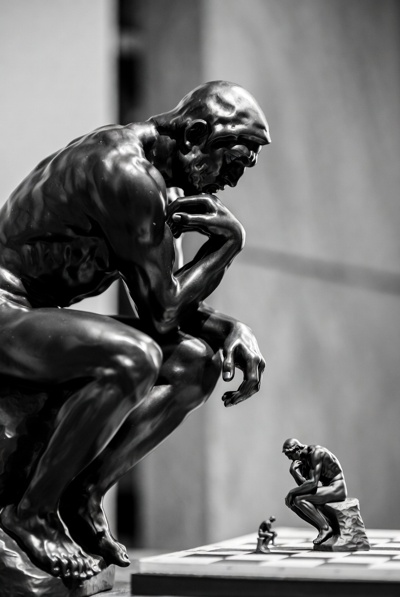 The Thinker contemplating a smaller Thinker on a chessboard — infinite regress of contemplative play
